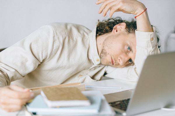 A young man with his head down on the desk, resting on his arm - he looks stressed out.